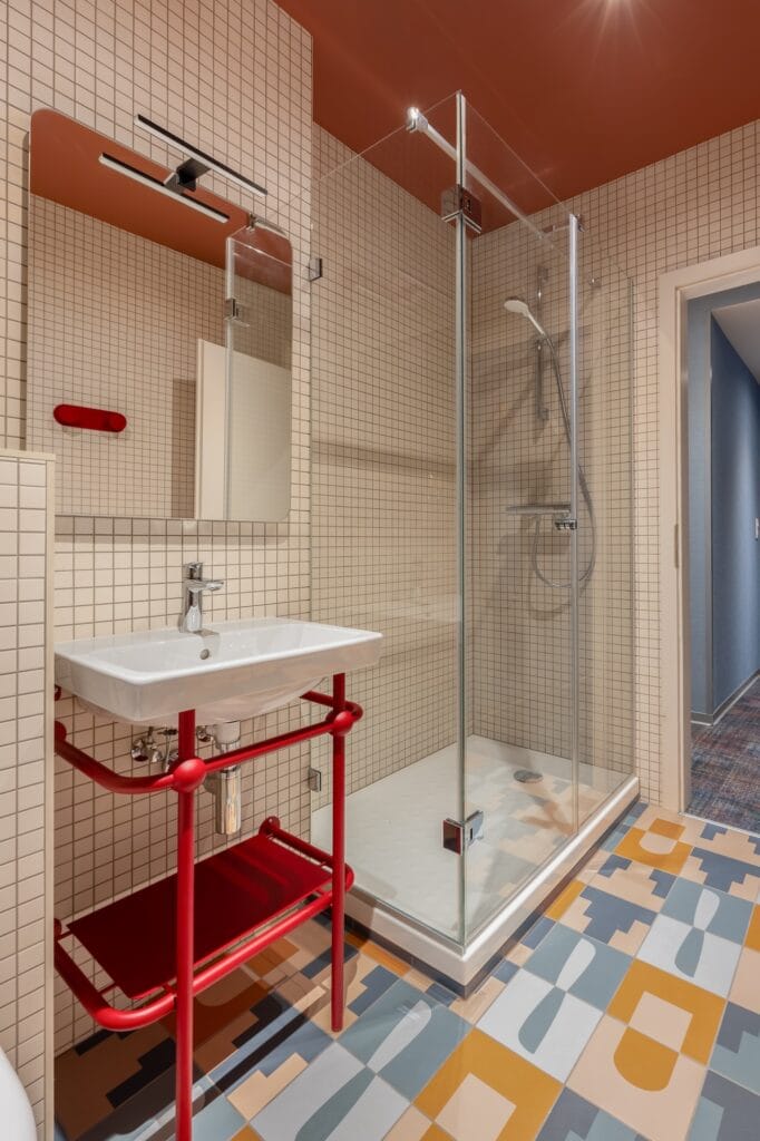 Vue sur la salle de bain avec piètement de lavabo rouge, douche vitrée, et carreaux de sol à motifs, par Etymodéco, Magali Brustlein, Directrice Artistique à Mulhouse en Alsace